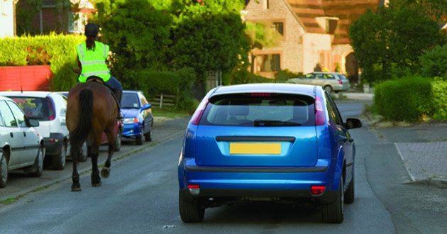 Car overtakes horse and rider, day.
