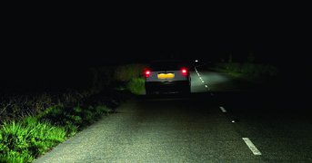 Car driving at night on quiet, poorly-lit road.