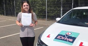 Charlotte stands holding her pass certificate beside car.