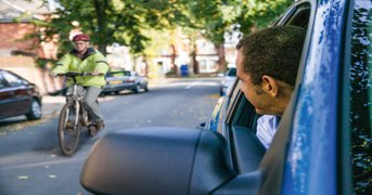 Driver with head out of window seeing passing cyclist in their blind-spot.
