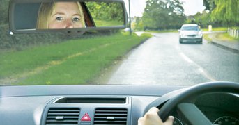 Young female driver eyes looking to camers in rear view mirror.