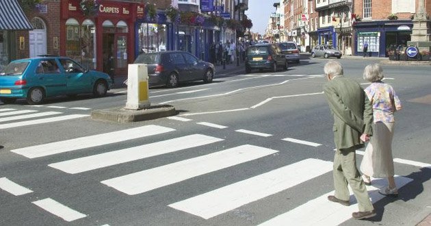 Elderly pedestrians step out onto crossing, day.