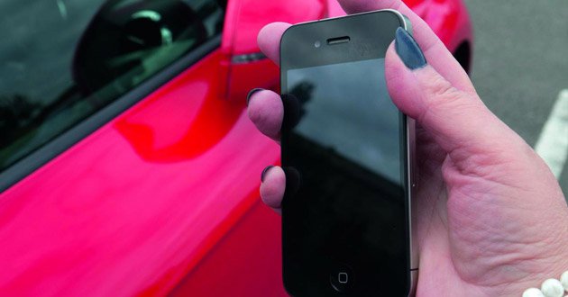 Hand holding a smartphone beside a parked car.
