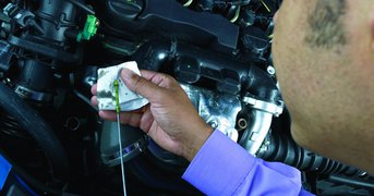 Oil dip stick held and checked against white cloth over engine.