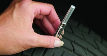 Female hand holding tyre-gauge against tyre to measure its pressure.