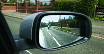 Motorcyclist behind car, captured in driver-side wing mirror.