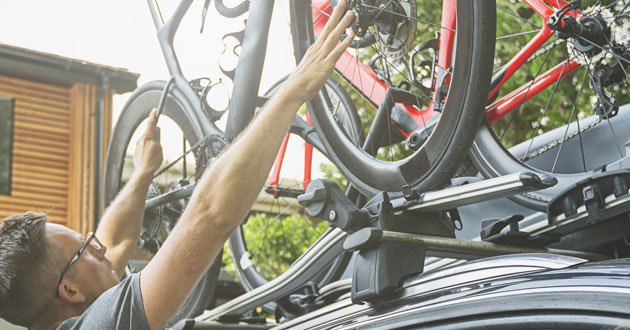 Man positions bikes beside roof-box on roof of car.