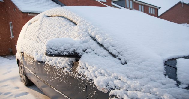 Snow-covered car, parked outside residence, day.