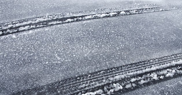 Car tyre track imprints through ice and slush covered tarmac.