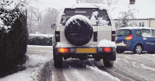 Off-road vehicle drives through hazardous wintry conditions on small road.